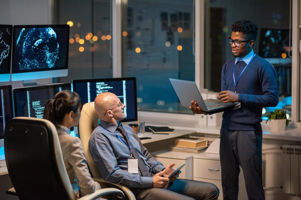 IT team reviewing data on a laptop beside cyber security monitors