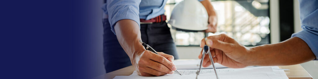 Engineer drafting architectural plans with a compass beside a hard hat