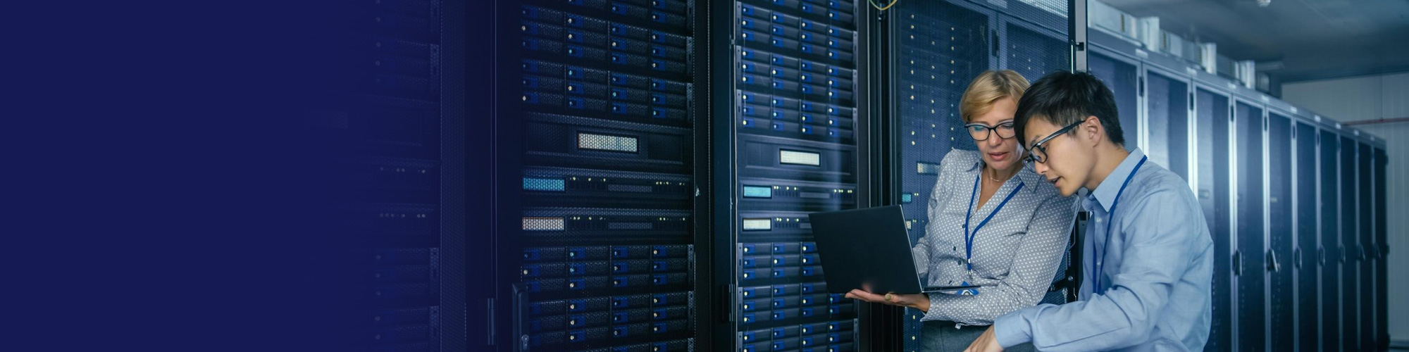 Two IT engineers reviewing a laptop between server racks in a data centre