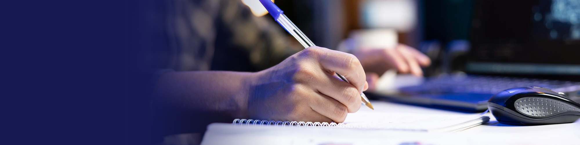 Person writing notes in a notebook beside a computer keyboard