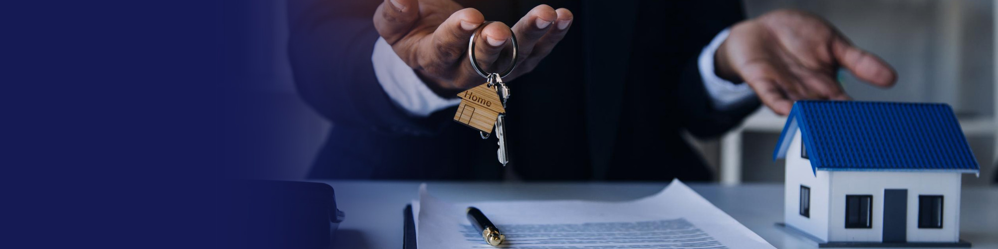 Real estate agent handing over house keys beside a contract and model home