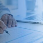 Person signing a document beside a laptop on an office desk