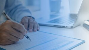 Person signing a document beside a laptop on an office desk